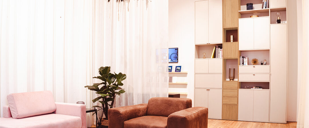 La décoration intérieure d'un salon avec un large fauteuil marrion et des étagères blanches.