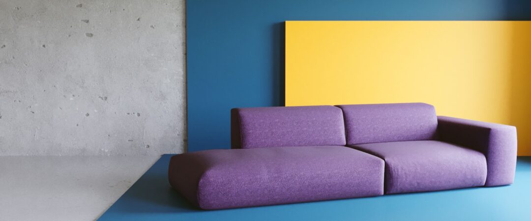 Un canapé violet sur un fond jaune et bleu rappelant les couleurs de la déco des années 80.