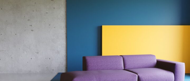 Un canapé violet sur un fond jaune et bleu rappelant les couleurs de la déco des années 80.