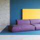 Un canapé violet sur un fond jaune et bleu rappelant les couleurs de la déco des années 80.